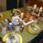 Table set with green tablecloth, gold chargers, fine china and crystal and Thanksgiving arrangement