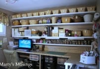 Small scrapbook room with picture of 8 foot counter with L side counter, computer, baskets on four shelves for storage and storage drawers underneath counter and embellishment storage in small jars.