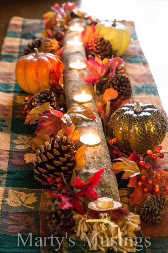 branch with holes cut out for tea candles and flowers, pinecones, acorns and fall decor arranged on top of table runner