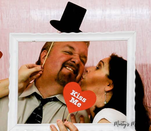 Husband and wife centered in empty frame with kiss me sign in photo booth