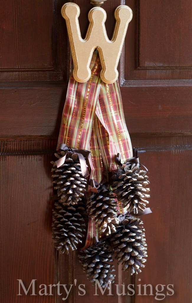 Pine cones grouped together with ribbon and a spray painted gold monogram 2, hung on front door