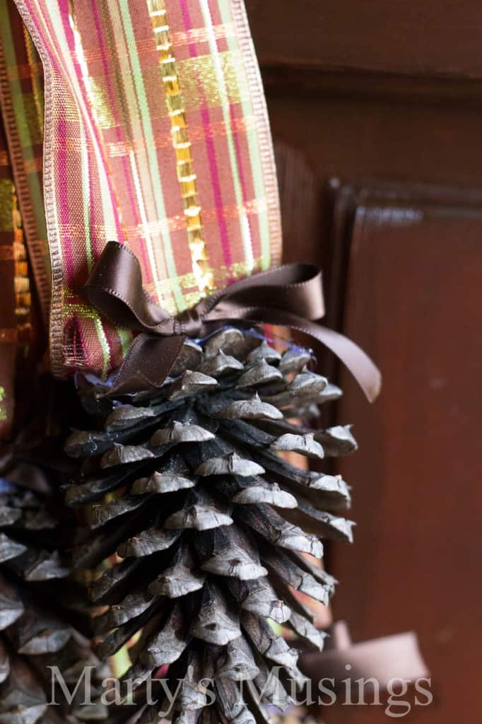 Single closeup shot of pinecone with brown ribbon attached to larger striped glitter ribbon