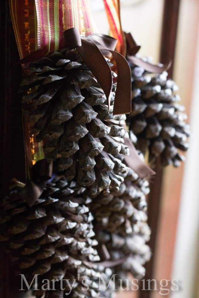 Group of pinecones photographed close up attached by small ribbon ribbon to striped glitter ribbon and hung on a wooden door