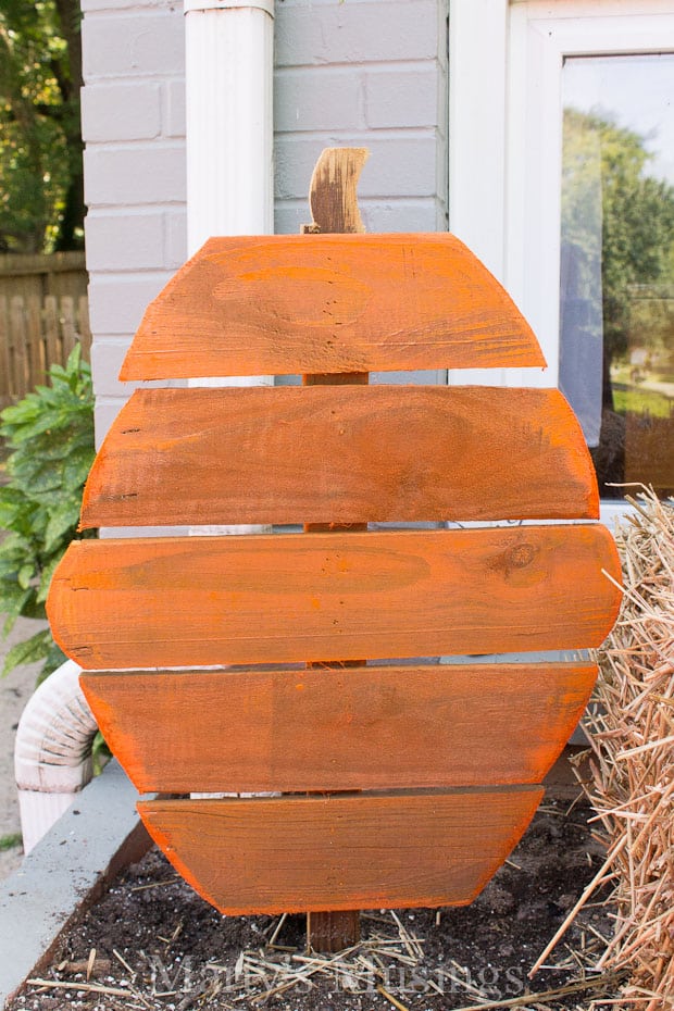 Orange scrap wood pumpkin in flower bed for fall