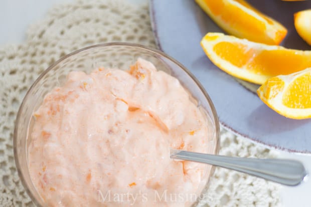 Orange jello salad in glass bowl with fresh oranges on blue plate