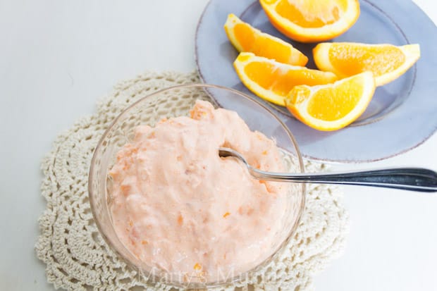 Orange jello salad in glass bowl with fresh oranges on plate