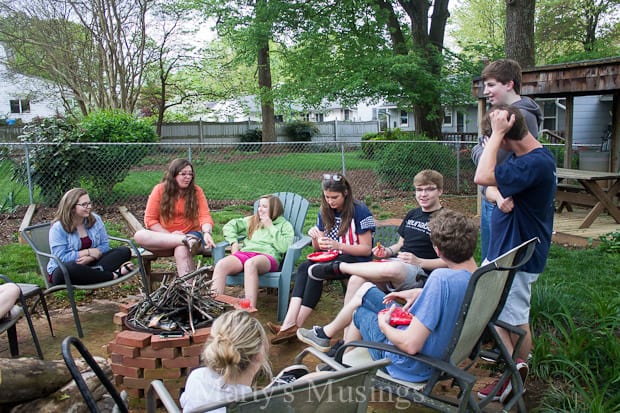 A group of youth sitting around a fire pit in backyard