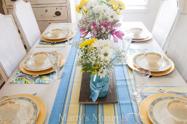 A table with a vase of flowers sitting on a plate, with Blue and Spring