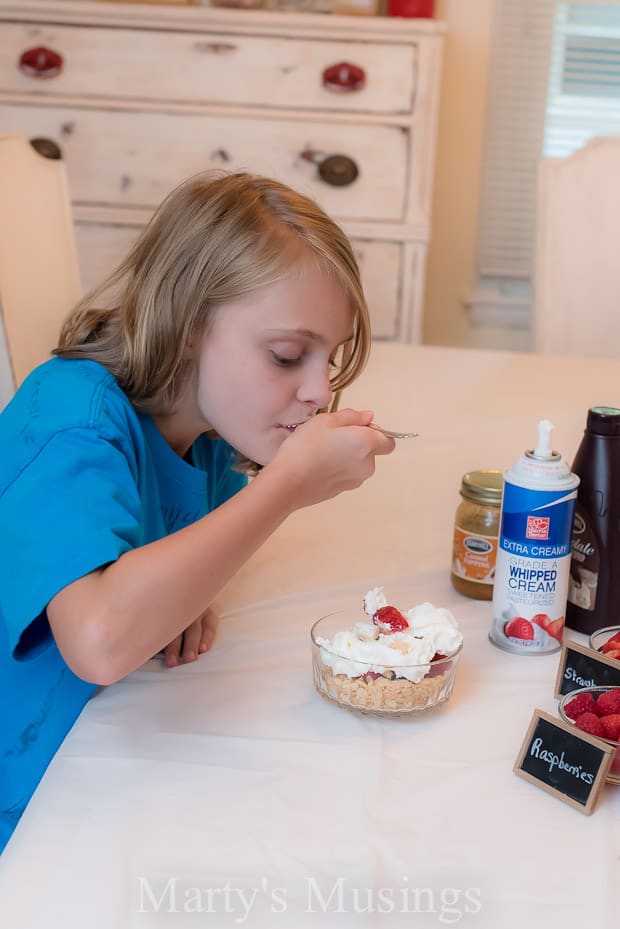 A little girl sitting at a table eating food, with Ice cream bar