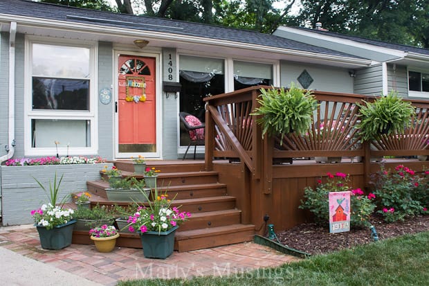 Front deck filled with planters of flowers, hanging ferns and rose bushes