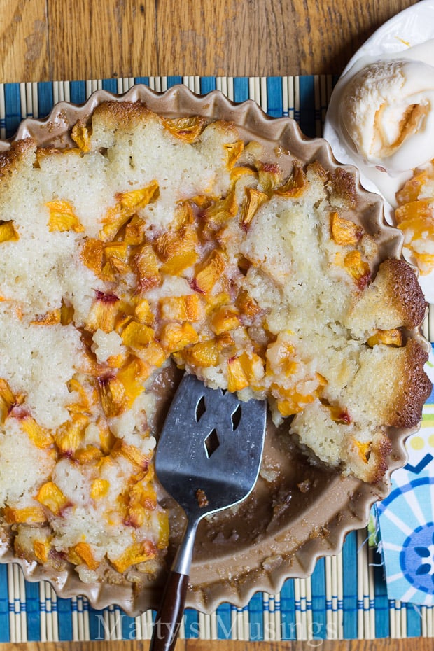 Peach cobbler in pie pan with vanilla ice cream on blue place mat