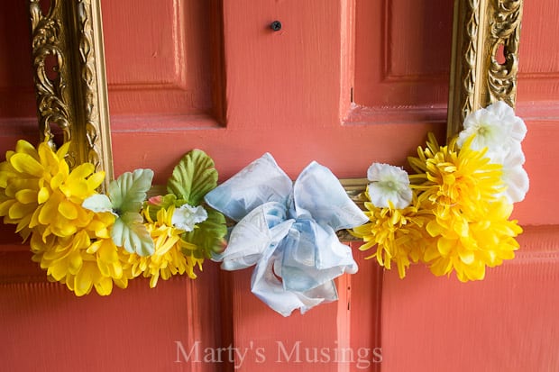 Create a warm welcome for guests with this easy and inexpensive front door wreath using a repurposed yard sale picture frame, silk flowers and wooden sign.