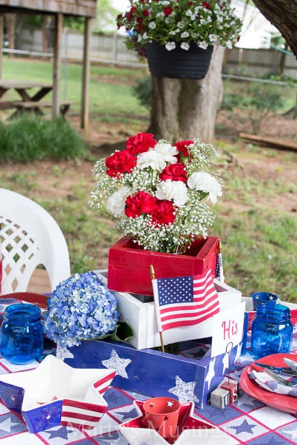 Inexpensive 4th of July table decorations from yard sales, thrift stores and around the home with seasonal flowers create a perfect rustic, outdoor setting.