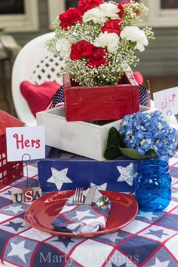 Inexpensive 4th of July table decorations from yard sales, thrift stores and around the home with seasonal flowers create a perfect rustic, outdoor setting.