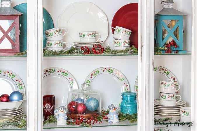 White china hutch filled with Christmas china and greenery
