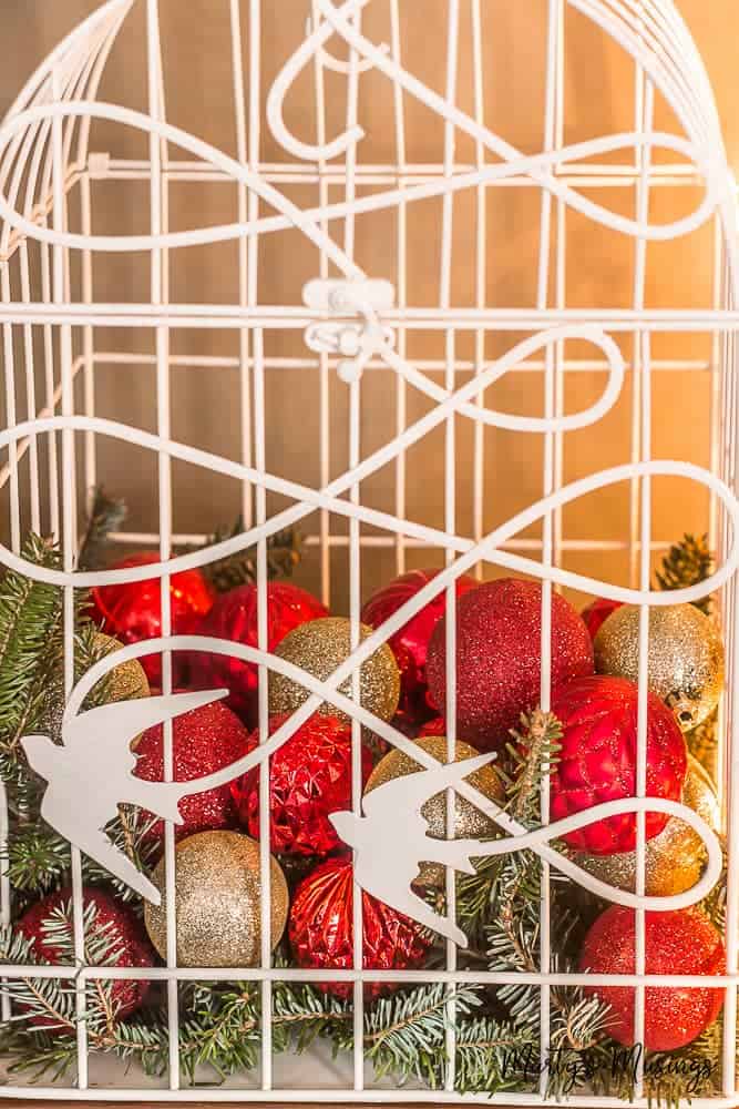 Bird cage filled with glittery Christmas ornaments and greenery