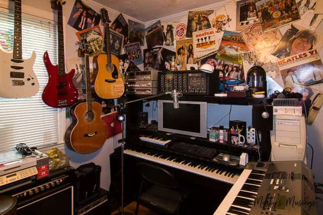 A piano keyboard with guitars and album covers hung on wall