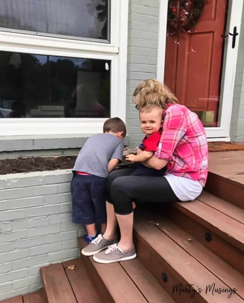 Grandmother helping her two grandsons outside front door of house