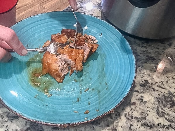 A blue plate of barbecue being shredded with forks