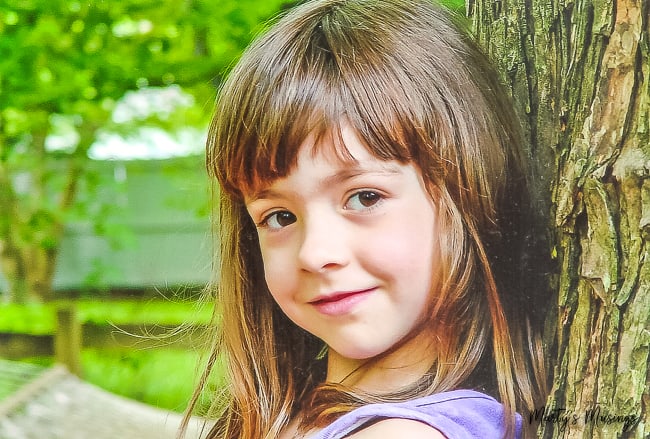 young girl with long brown hair leaning against tree