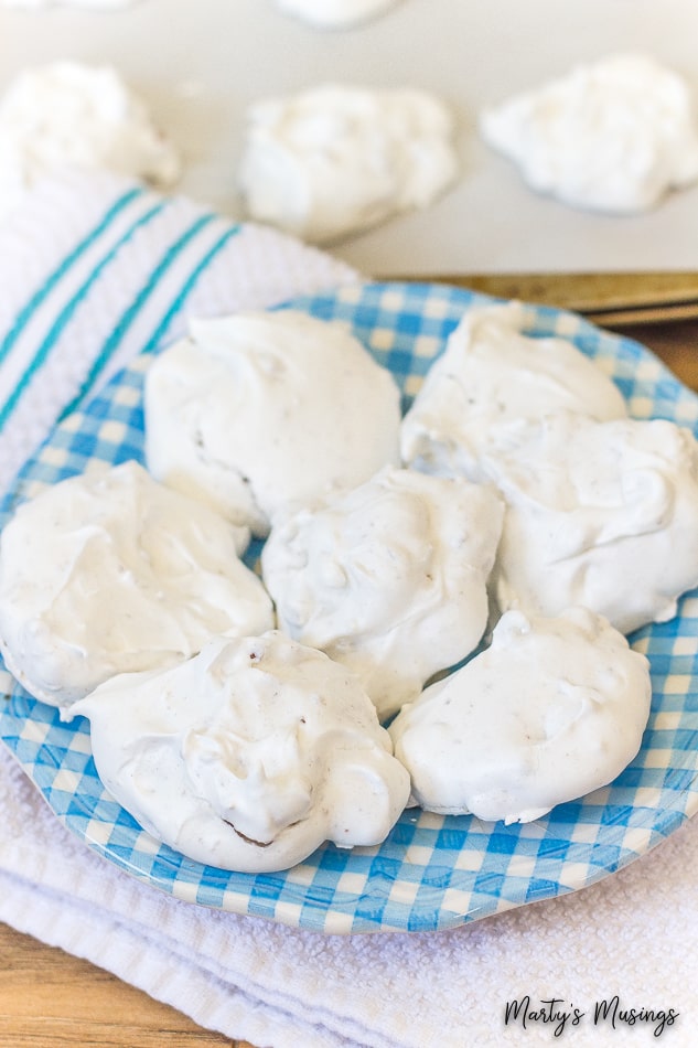 White meringue cookies on blue plate with cookies on baking sheet