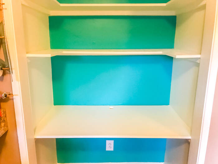 White plywood shelves and desk in closet with teal back wall