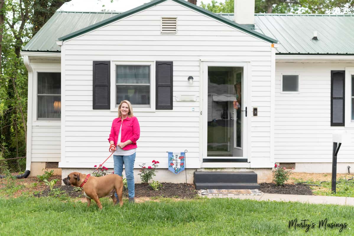 woman in pink jacket outside white cottage with dog on leash