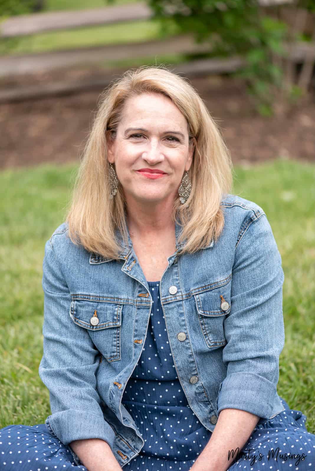 woman in blue polka dotted dress and jean jacket sitting in grass