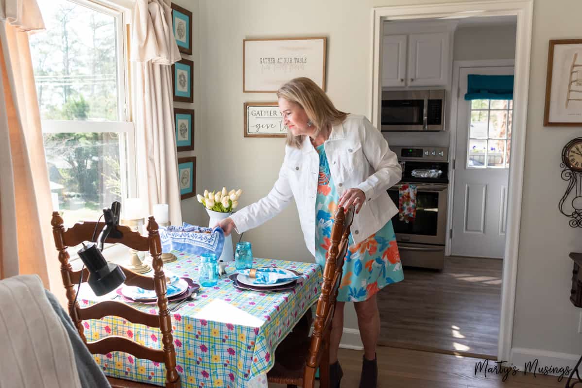 woman in floral dress and white jacket setting a small dining table