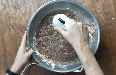 Hand held mixer stirring ingredients in metal bowl