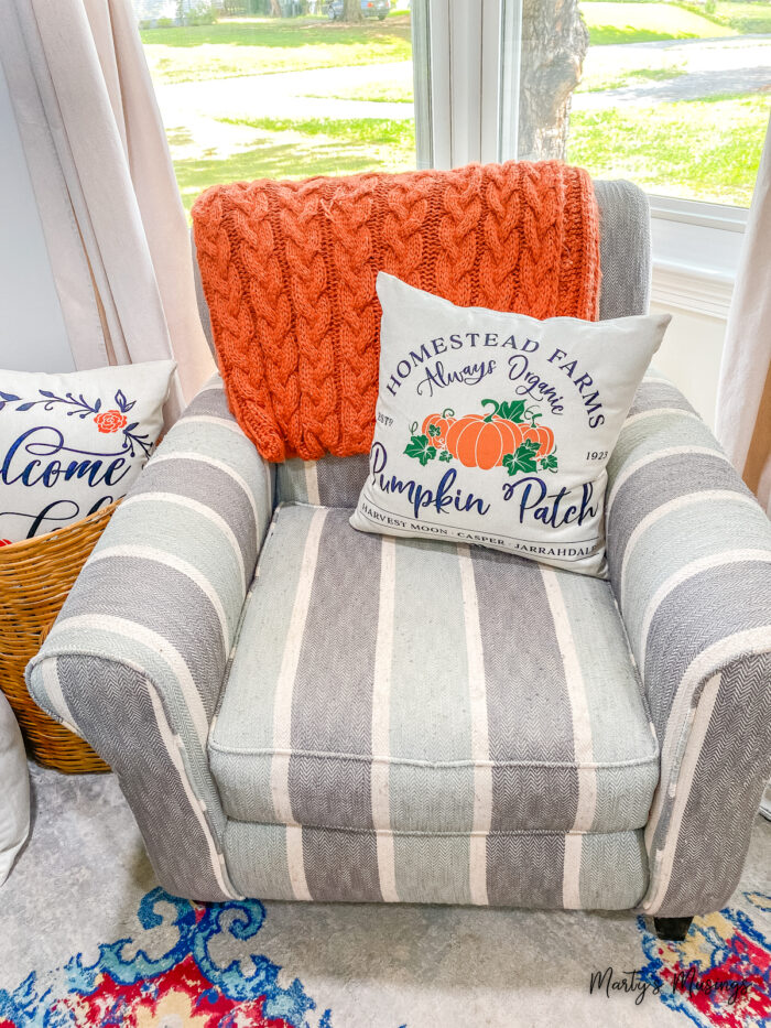 Blue and gray striped chair with orange throw and pumpkin patch pillow
