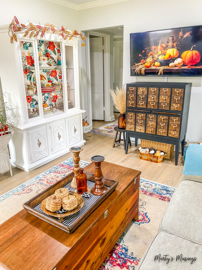 Small living room with white china hutch and vintage card catalogue decorated for fall
