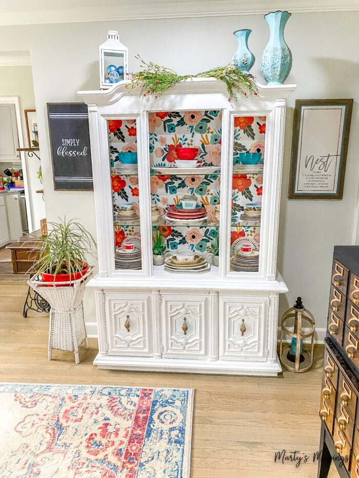 White china hutch with floral wallpaper inside