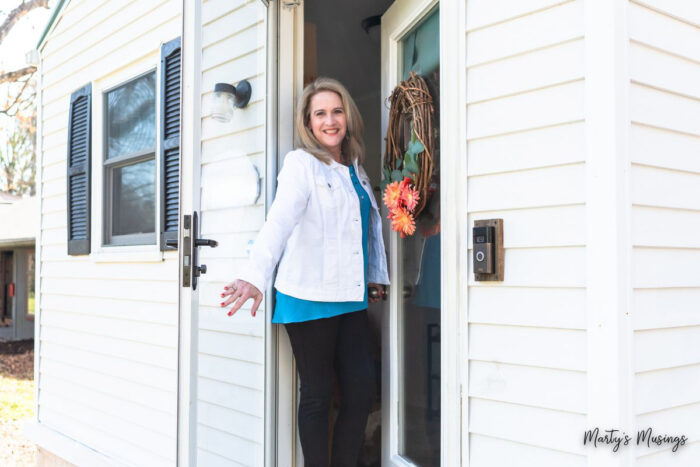 Woman in white jack and blue shirt opening front door