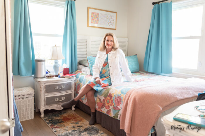 Woman in floral dress and white jacket sitting on bed