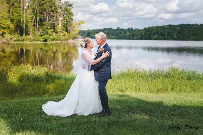 Older bride and groom in white full length wedding gown and navy blue suit in front of lake.